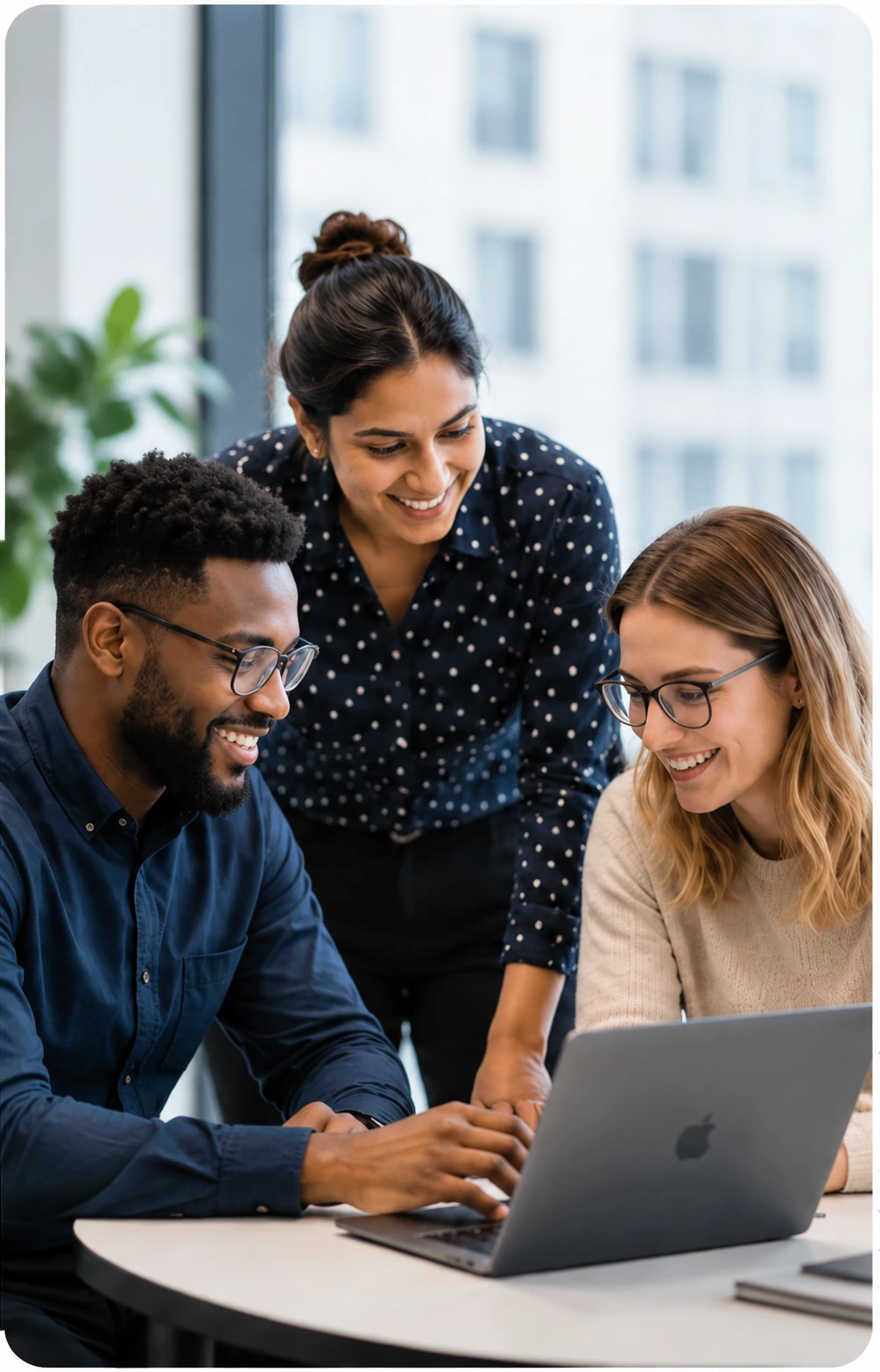 Three colleagues gathered around a laptop by a window