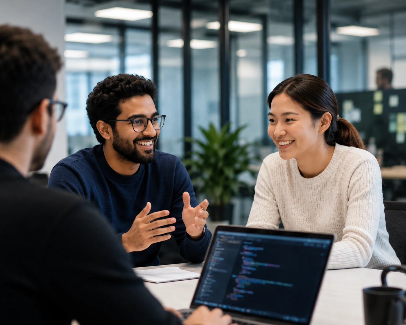 Three colleagues talking around a desk in a glass-walled office